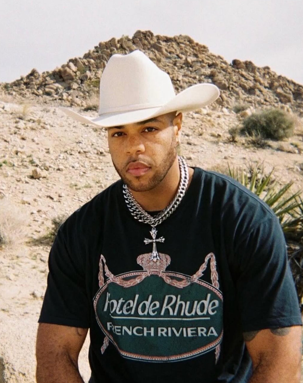 AX Rated wearing a cowboy hat and 'Hotel de Rhude' t-shirt in a desert setting
